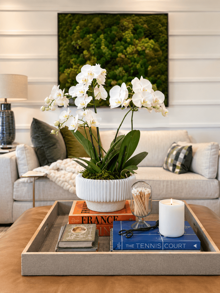 Coffee table styled with a white orchid in a fluted planter, stacked books and a candle on a linen tray