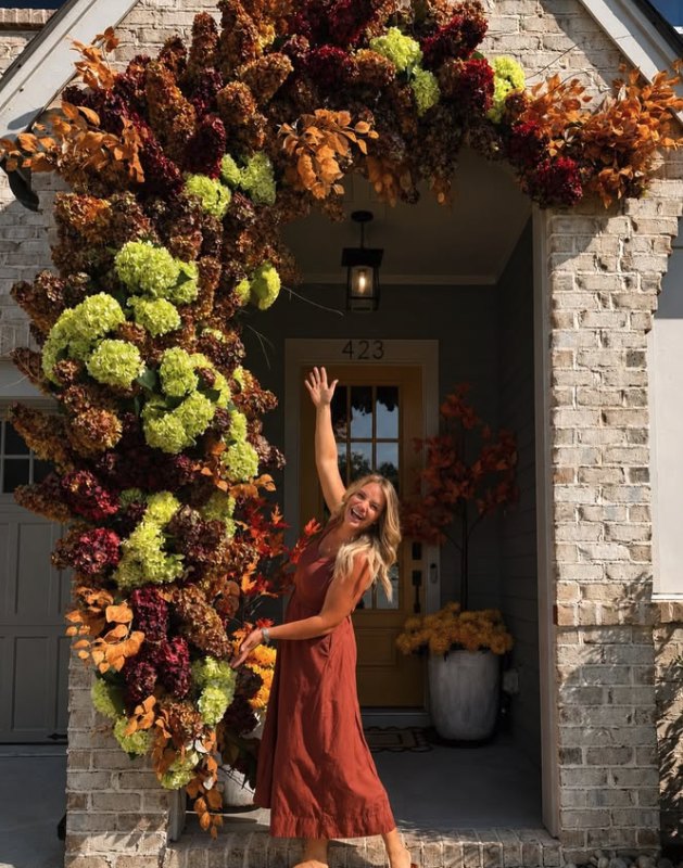 Gina standing in a doorway framed by her fall floral installation